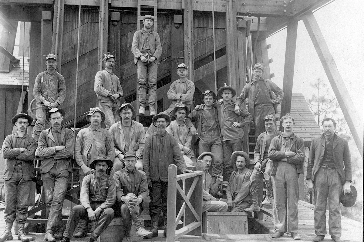 Black-and-white group portrait of workers standing and sitting on wooden steps and platforms outside River Hill Mill.